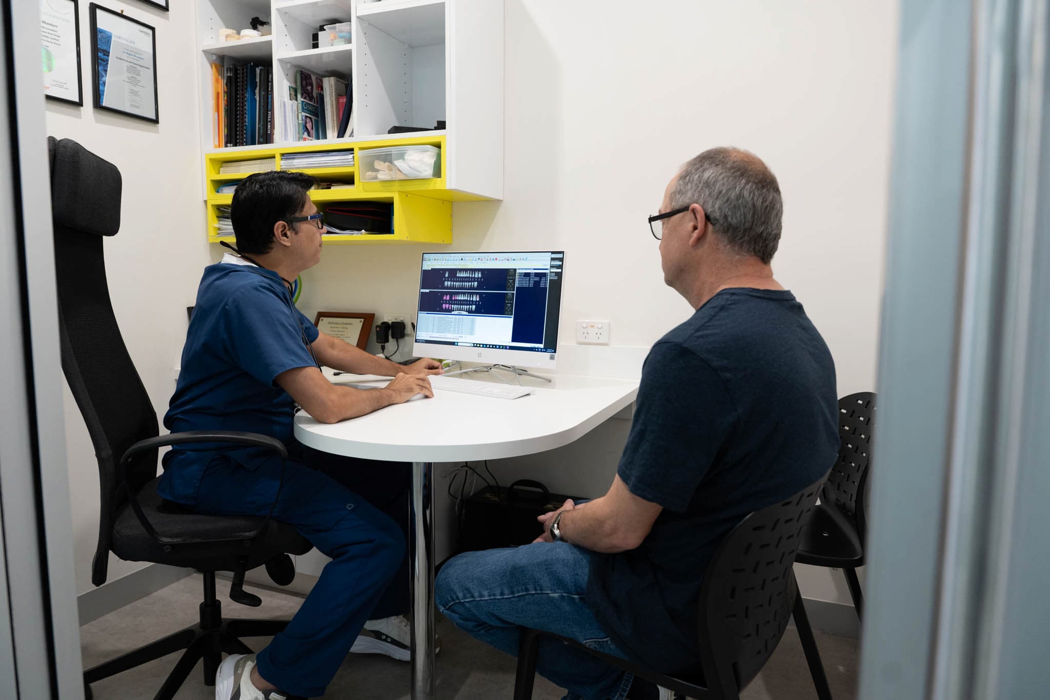 Dentist consulting with patient while reviewing digital dental X-rays on screen.