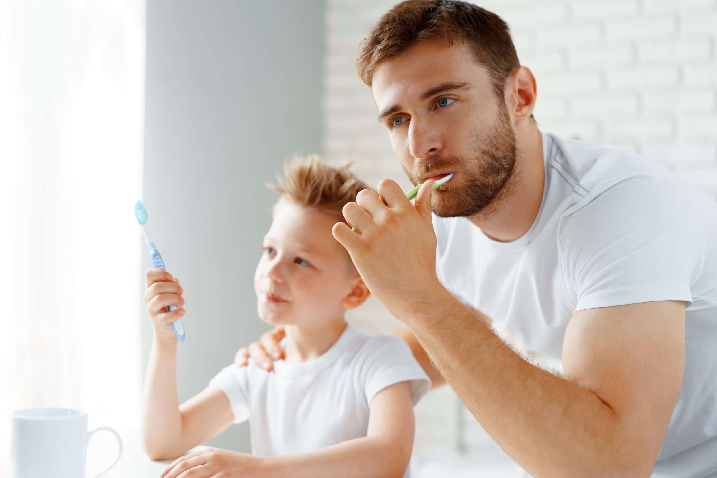Father and child brushing teeth together at home for healthy oral hygiene.