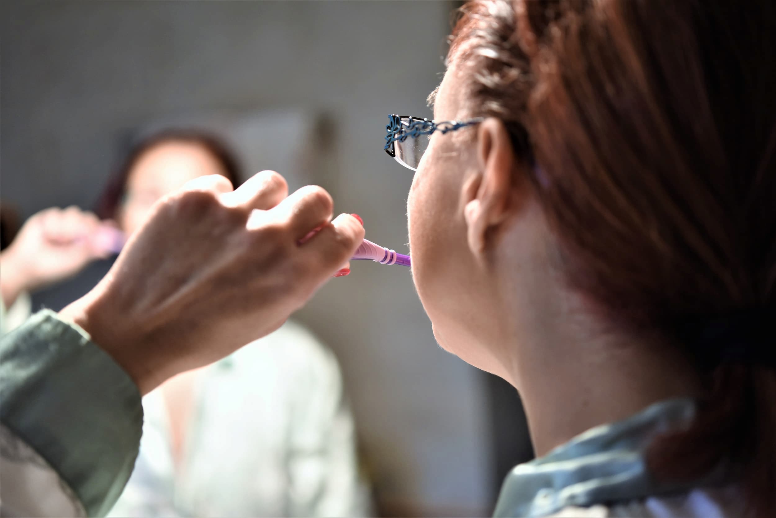 Woman brushing her teeth in the bathroom mirror.