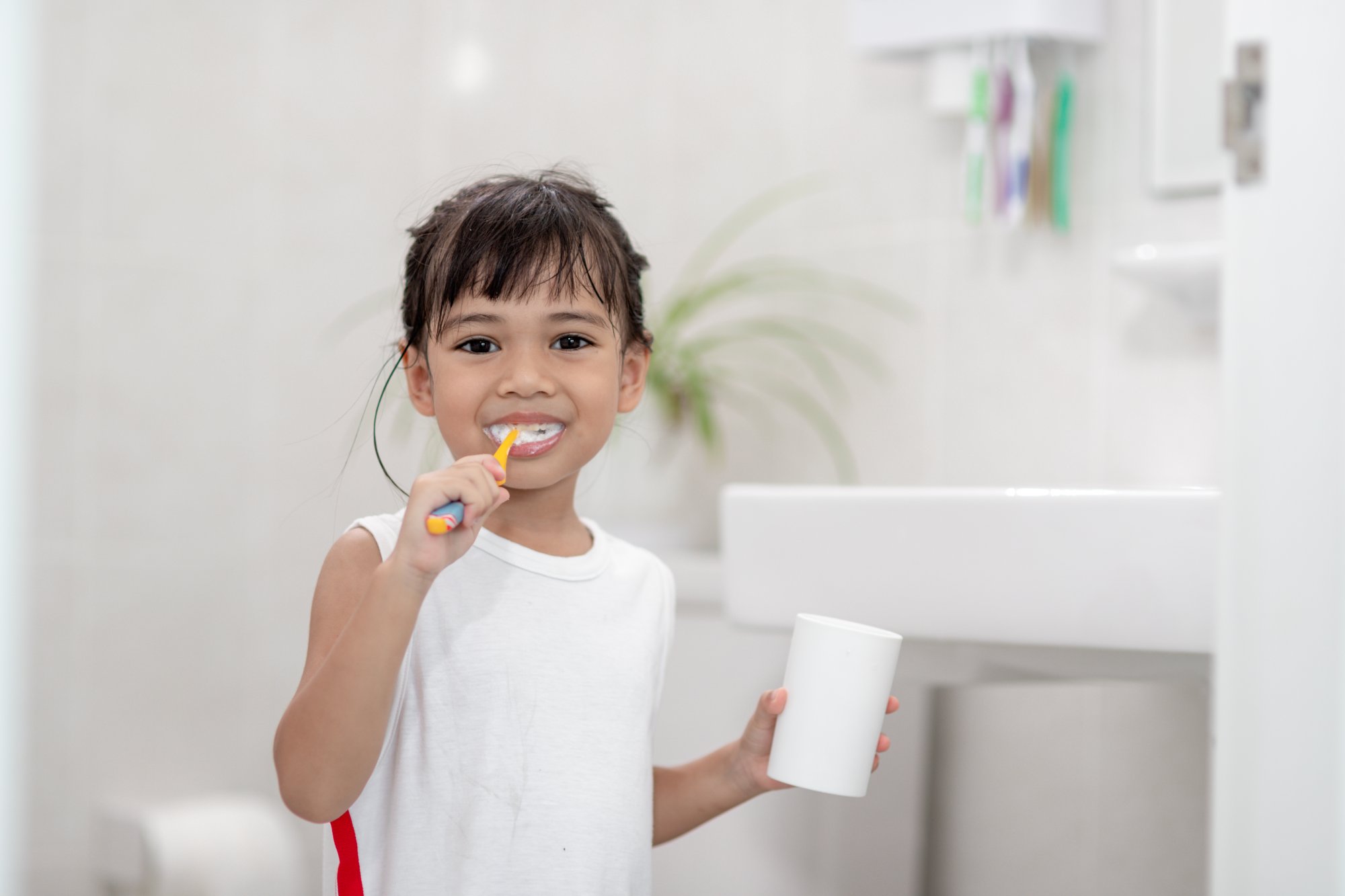 Young girl brushing teeth holding a cup