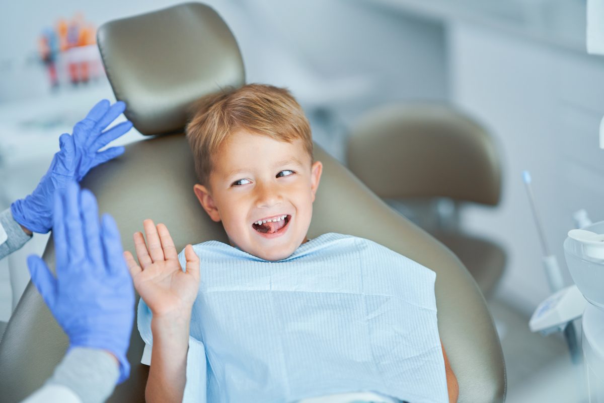 Happy young boy giving high five to dentist at Exquisite Smiles Warner